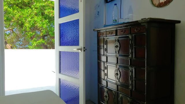 Antique Chinese Apothecary Dark wooden cabinet, indoor bedroom with green trees outside. Vintage