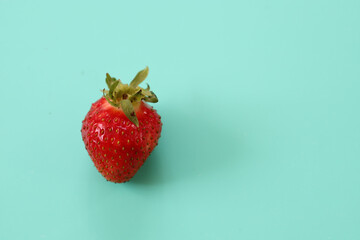 A single fresh, bright red strawberry with a green stem is placed on a clean turquoise background....