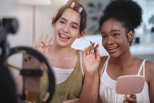 Two girls of different ethnicities and skin tones are live streaming a makeup tutorial for social at home, beauty influencer makeup artist.