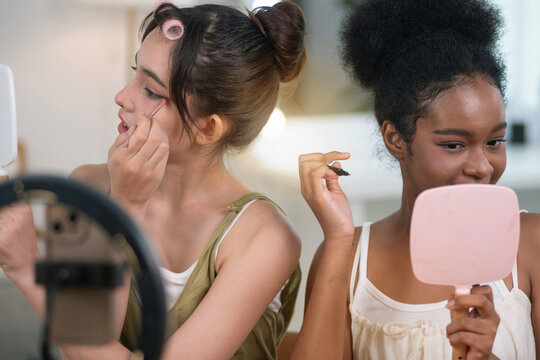 Two girls of different ethnicities and skin tones are live streaming a makeup tutorial for social at home, beauty influencer makeup artist.