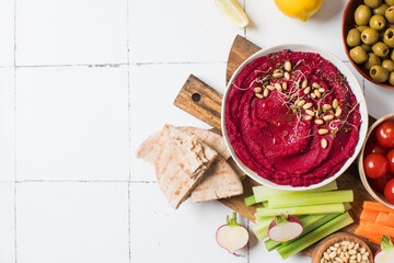 Beetroot hummus in a bowl on a board with fresh vegetables, celery, carrots, pita. Copy space