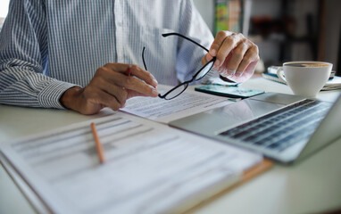 asian businessman holding eyeglasses working and meeting online with business group via laptop on desk at home office, working at home concept