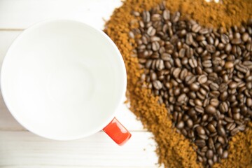 Flat design white ceramic mug with red handle is resting beside roasted bean heart, grounds