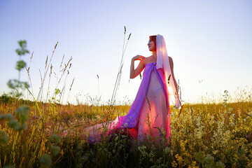 Model in flowing dress poses gracefully in a vibrant field during sunset