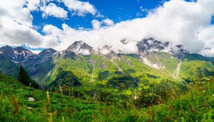 A stunning view of green mountains beneath a bright blue sky with fluffy white clouds. This image...