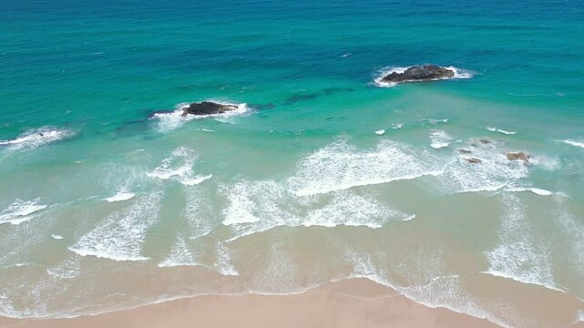 Looking down at the clear water crashing in on the golden sand.
