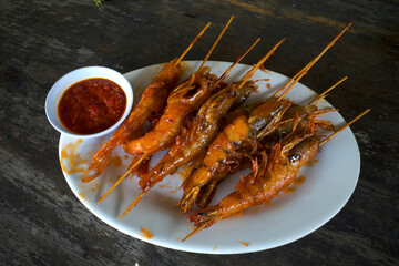 Shrimp satay with chili sauce at white plate on an old wooden table