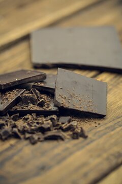 Naklejki Dark chocolate squares and shards are lying on wooden table in flat design, with crumb fragments