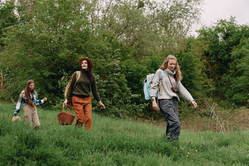 Obraz premium Middle age woman hiking outdoors with two younger women, enjoying active lifestyle, wellness, health, and nature in a green forest setting during spring season.