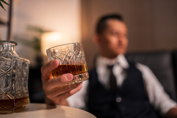 Asian businessman sitting and drinking whiskey in a room on a sofa.	