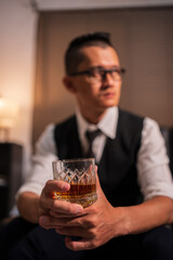 Asian businessman sitting and drinking whiskey in a room on a sofa.	