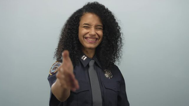 Hispanic policewoman in uniform extends a handshake, smiling confidently against a white background.