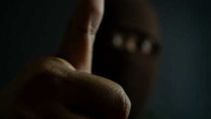 Masked man in brown eye-only cloth mask giving thumbs up, blurred face with clear hand gesture,...