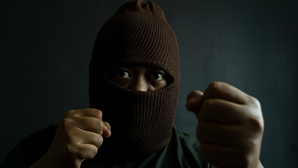 Masked man in brown cloth mask striking a fighting pose, clenched fist raised with eyes visible,...