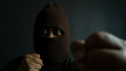Masked man in brown cloth mask striking a fighting pose, clenched fist raised with eyes visible,...