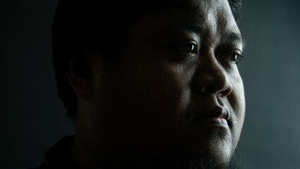 Bearded Indonesian man on black background, neutral expression in low-key lighting, simple portrait...