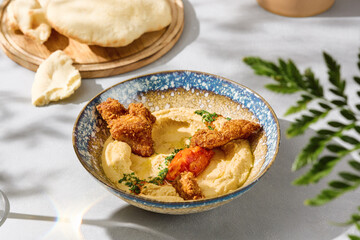 Hummus with chicken strips and pita in bright natural light, overhead rustic composition