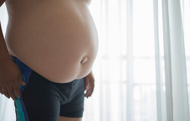 Fat man holding his belly at home. Close up of overweight man with fat belly.