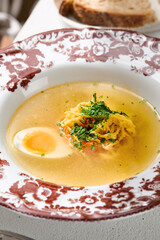 Chicken broth with egg and noodles, bright natural lighting, overhead plated composition