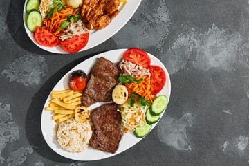 Beef steaks with fries, rice and vegetables, bright rustic lighting, overhead composition