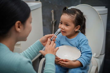 mother making nasal wash for happy toddler girl with syringe and saline. cleaning nose