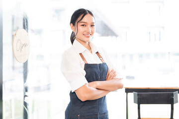 Portrait of smiling waitress standing with arms crossed at her shop