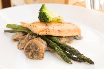 dish of fried river trout fillet with garnish of broccoli, asparagus sprouts and mushroom sauce on white background
