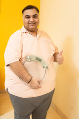 Overweight obese indian man holding weight machine. Plus size fat guy weight loss concept. Obesity.