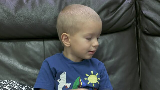 Child playing with new toy sitting on sofa at home. Concentrated face of little boy holding transformer robot toy. Three year old child examining new toy comments on his actions.
