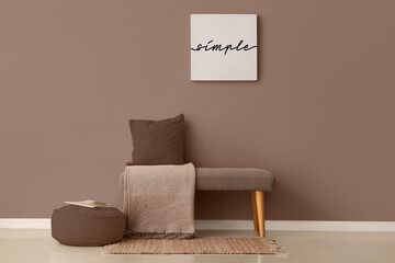 Grey bench with cushion, blanket and pouf near brown wall