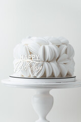Birthday cake covered with white edible paper petals and decorated with golden Happy Birthday topper. White background