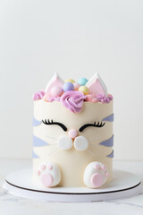 Cute birthday cake in the shape of cat with mastic ears and paws decorated with pink cream fur on the white background. Adorable cake for a little girl who likes cats