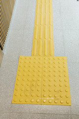 Tactile paving surface with yellow bumps for the visually impaired, close-up of textured warning...
