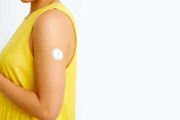 Woman wearing continuous glucose monitor attached to the upper part of her arm. Space for text
