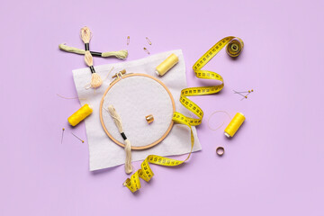Embroidery hoop with canvas, mouline threads and measuring tape on lilac background