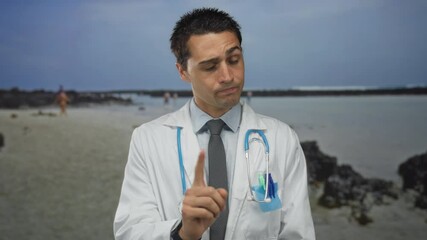 Doctor wearing stethoscope and white coat pointing finger to camera in studio with serious expression; warning.