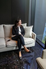 Obraz premium In a modern office, a confident businesswoman relaxes on a stylish couch, embodying professionalism and sophistication while radiating positive energy that brightens the atmosphere