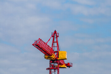 Naklejka premium Red and yellow construction crane against cloudy sky.