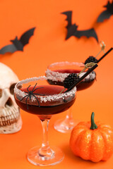 Glasses of delicious cocktail for Halloween with blackberry and pumpkin on orange background, closeup