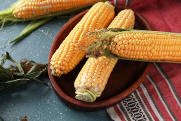 Bowl with fresh corn cobs on blue table