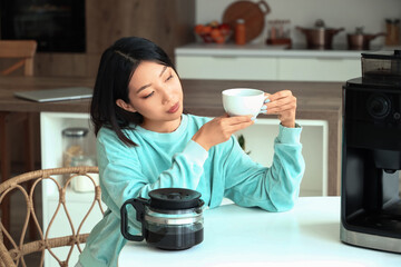 Beautiful Asian woman with cup of hot coffee in kitchen