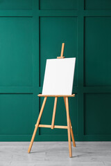 Wooden easel with blank canvas near green wall