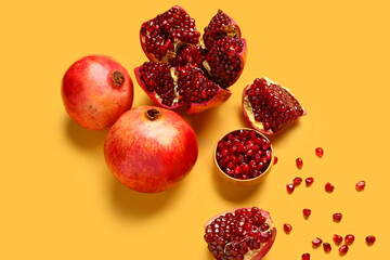 Fresh pomegranates and bowl with seeds on yellow background
