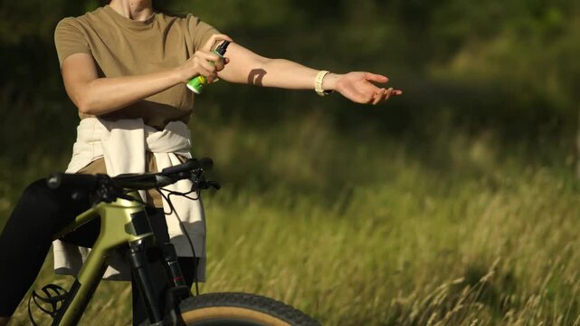 Woman sprays insect repellent on arm near her bicycle outdoors