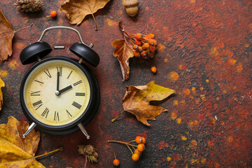 Alarm clock with viburnum and autumn leaves on grunge background