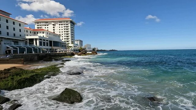 waves crashing on the shore of old san juan puerto rico with tall hotel building in the background (caribbean travel tourism destination) sj pr sea coast rocky shore beach condado
