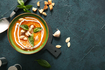 Bowl of delicious pumpkin cream soup with seeds and basil on dark background