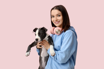 Beautiful young woman with headphones and cute staffordshire terrier puppy on pink background