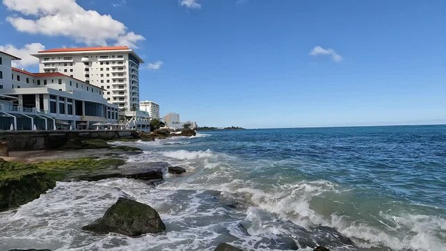 waves crashing on the shore of old san juan puerto rico with tall hotel building in the background (caribbean travel tourism destination) sj pr sea coast rocky shore beach condado