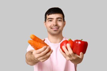 Young man with vegetables rich in vitamin A on light background, closeup